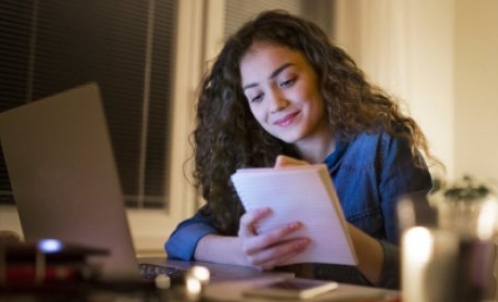 A high school student writing in a notebook at their desk